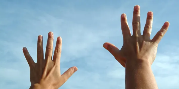 Two hands raised to a clear blue sky